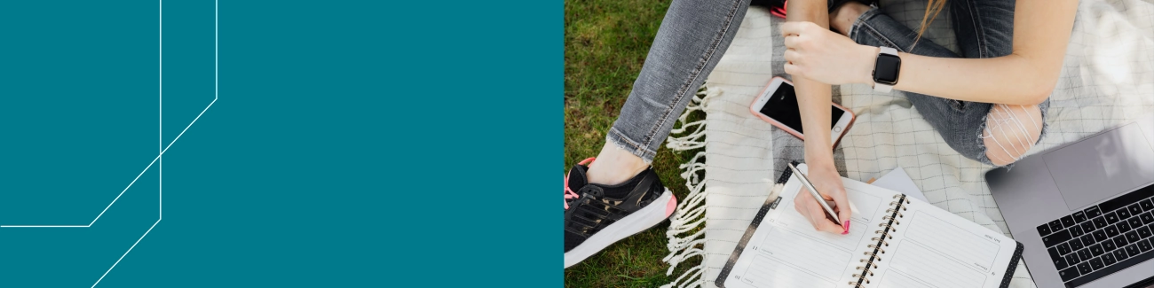 Nurmikolla työskentelevä naisoletettu: läppäri ja muistiolehtiö.