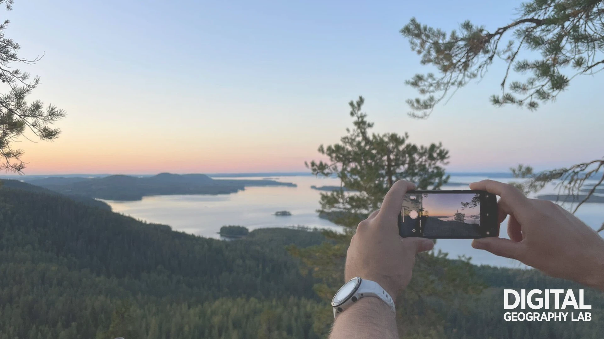 A person photographs a view from Koli National Park with a smartphone.